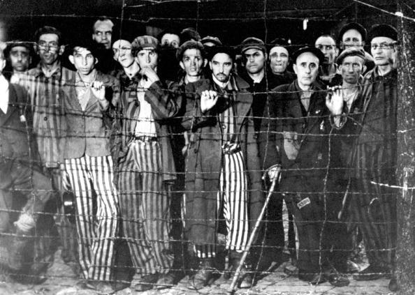  The Liberation of Buchenwald, 1945: Gaunt, hollow-eyed concentration camp survivors grip barbed wire fence and stare in wonderment during their liberation