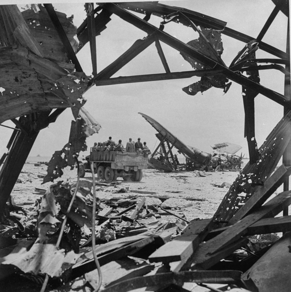  1944: Truck loaded with 2nd Division Marines drives past ruins of destroyed planes following an attack on a Japanese seaplane base in Saipan