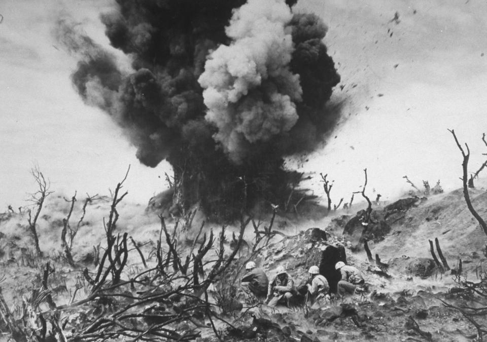  US Marines take cover behind a hillside rock as a Japanese blockhouse on Iwo Jima is detonated