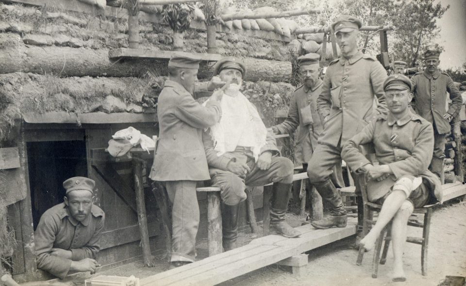  A soldier sits outside his trench while a colleague gives him a shave