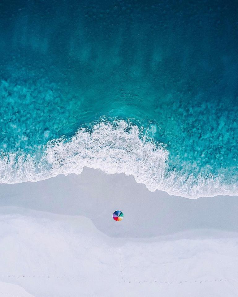 A lone beach umbrella is stark against the white sands and aquamarine sea of Carrickalinga