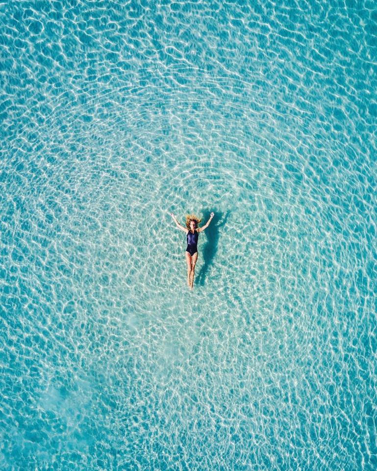 A swimmer appears suspended vertically in the cool blue ocean of Silver Sands, Aldinga Beach, when captured from directly above