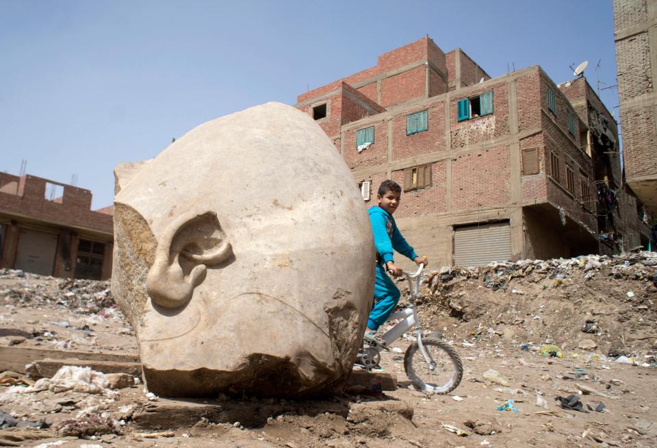 A boy rides his his bicycle past the head of the recently discovered statue