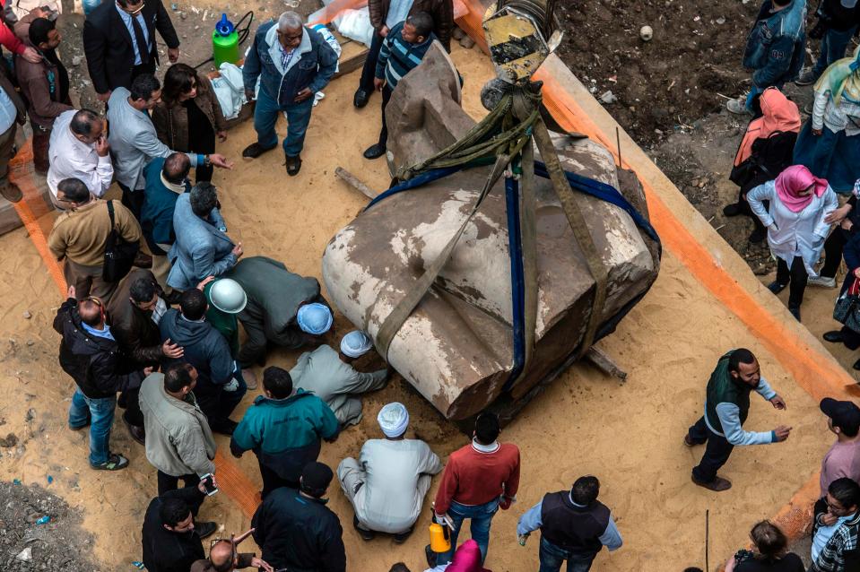 The ancient stature's torso is carefully lowered to the ground