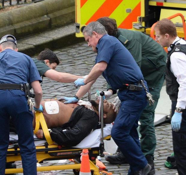 Khalid Masood lies on a stretcher outside Parliament with paramedics treating his injuries while armed cops stand guard