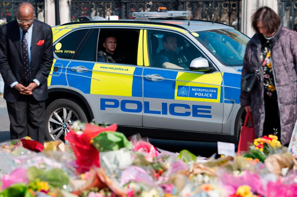  A police vehicle passes people as they look at floral tributes to the victims of the March 22 terror attack, near the Houses of Parliament in Westminster