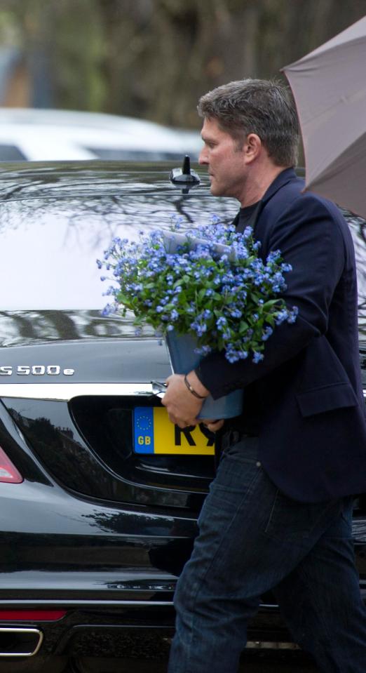  Kenny Goss carries a bunch of flowers as he makes his way to the wake at George's home