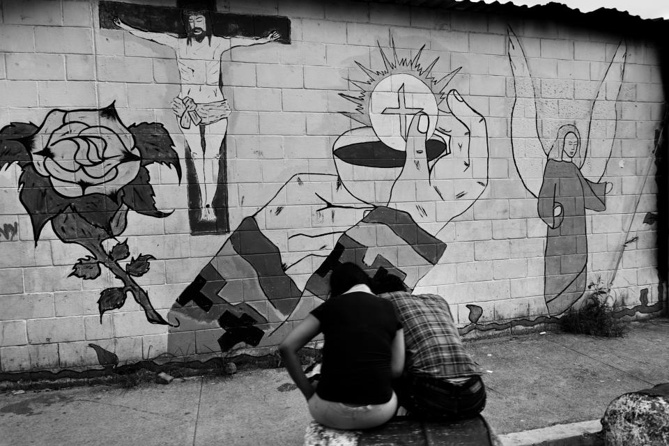  Young people sit in front of the religious murals painted on the wall in the gang neighbourhood