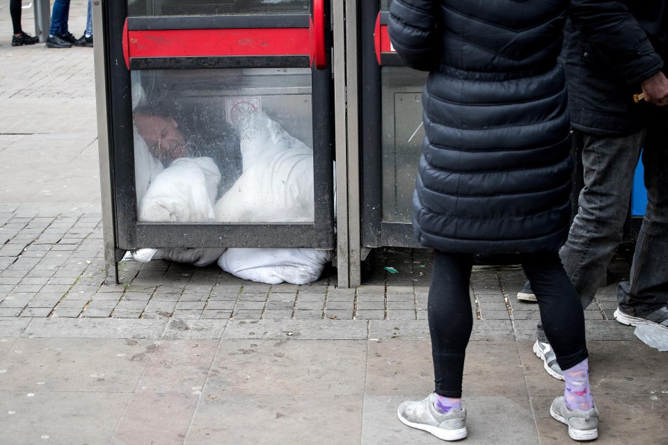 A man lies curled up on the floor of a telephone box after smoking a cigarette believed to contain spice