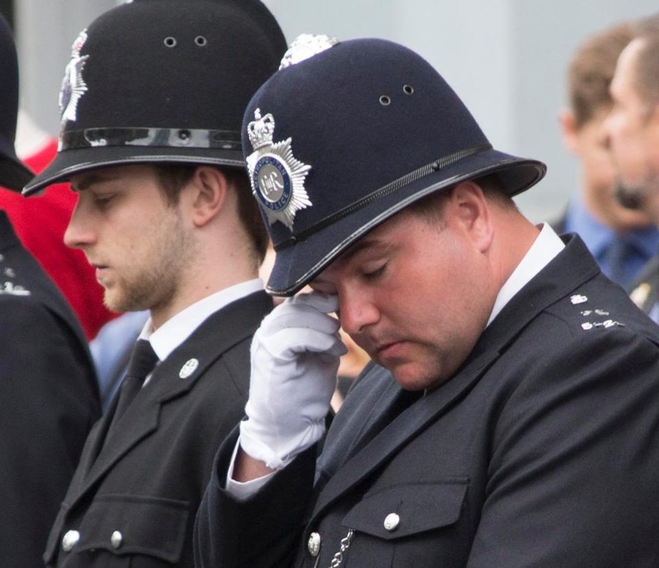 A police officer wipes his eye while the coffin is carried to the service 