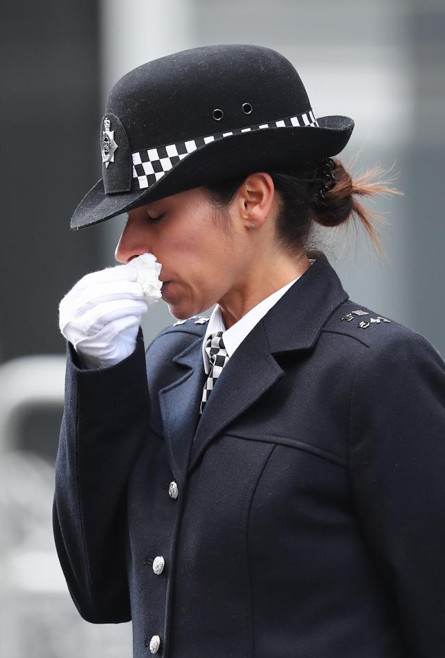 A female officer wipes away her tears with a tissue while wearing white ceremonial gloves