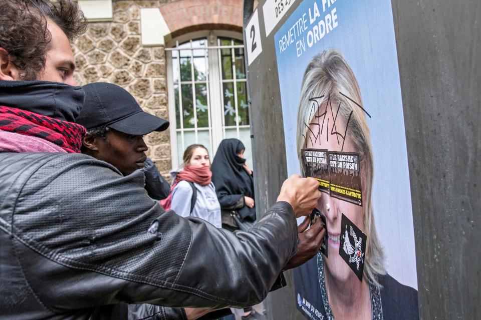  Protesters deface a campaign poster showing Marine Le Pen's face