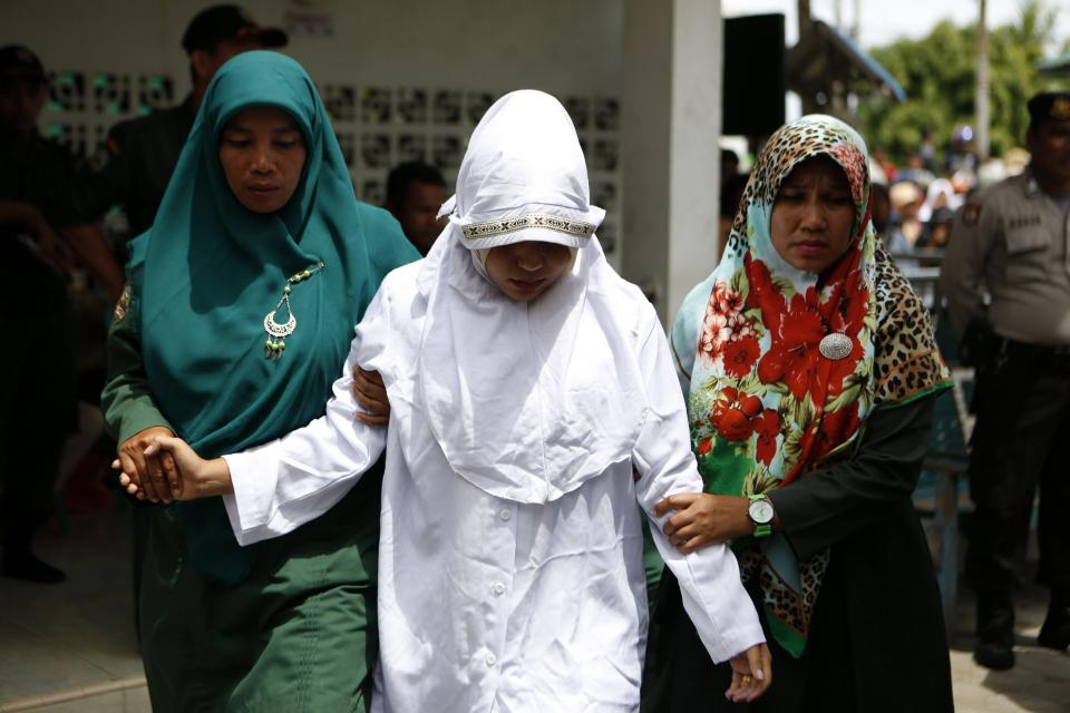  An Acehnese woman is escorted by sharia police as she is being whipped in public for violating sharia law in Banda Aceh, Indonesia