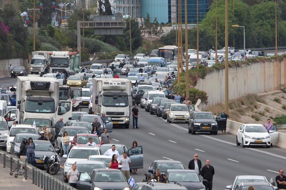  Israelis stand still next to their cars as a siren sounds in memory of victims of the Holocaust in Tel Aviv