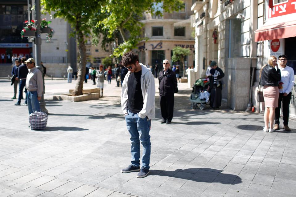  Israelis standing on a main Jerusalem street as a two-minute siren wails