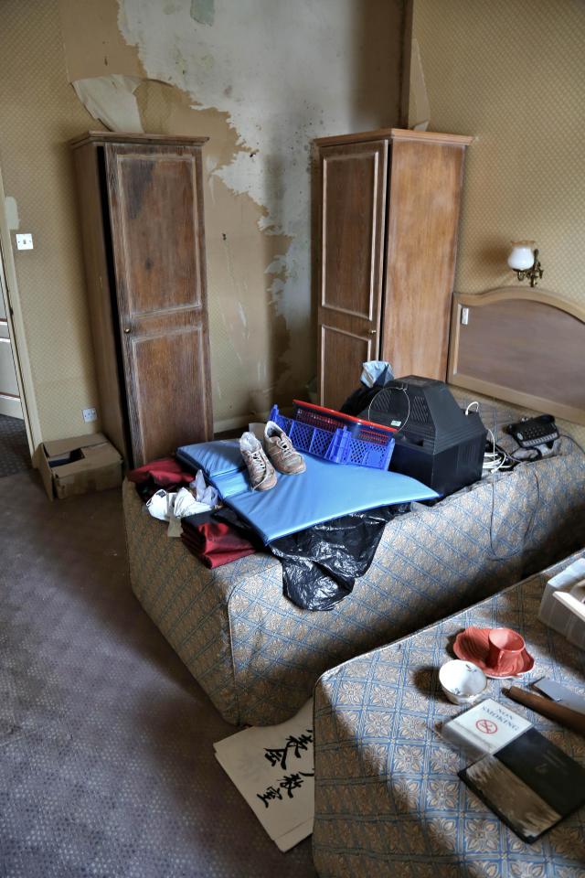  A TV lies face down on a bed in a room that features peeling wallpaper