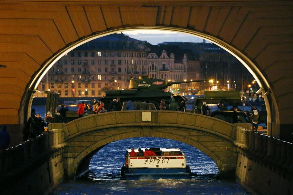  A massive tank casually trundles over a bridge as a tourist boat floats beneath