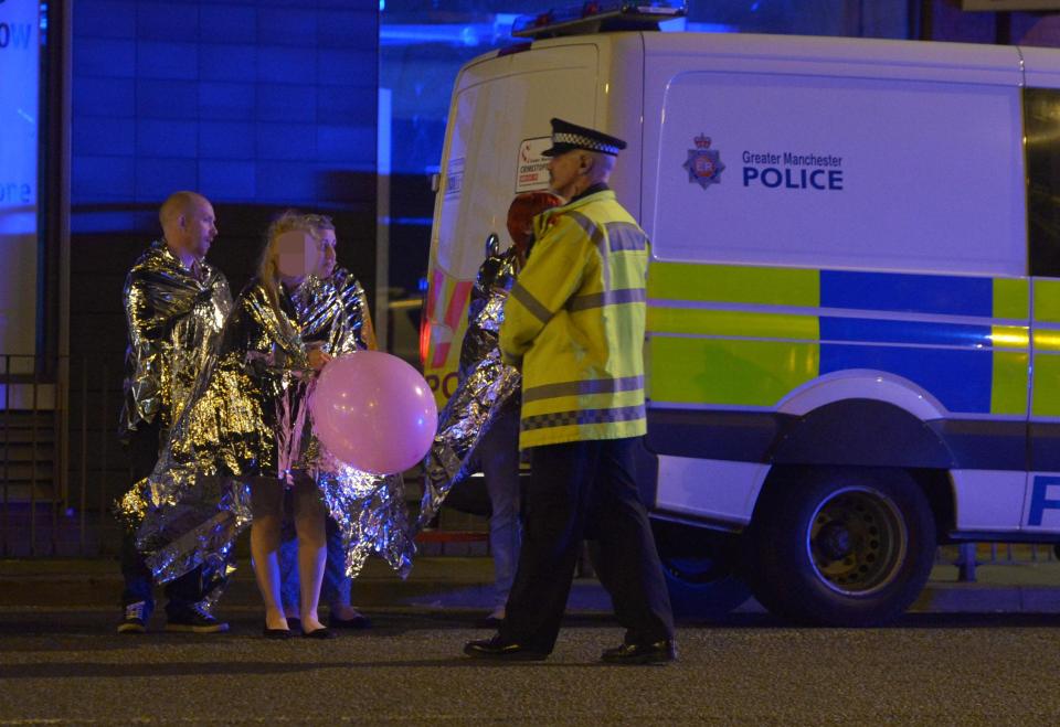  Stranded concert-goers wrapped in thermal blankets wait by police van after bombing