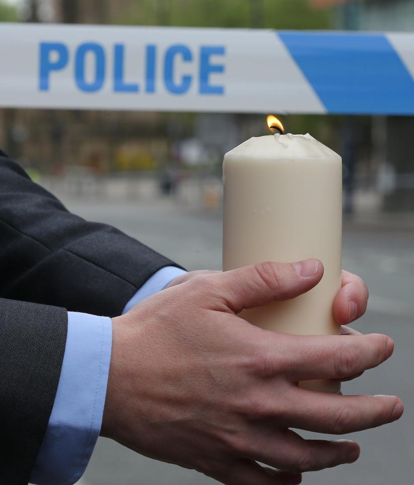 A candle is held near the police cordon as forensic investigators continue to scour the area for evidence