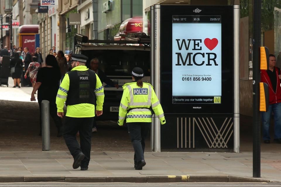 Two cops walk past another sign on an electronic billboard on a city centre street