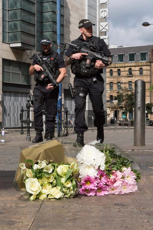 Heavily-armed police hold their guns next to bouquets of flowers left in memory of those killed in the terror attack