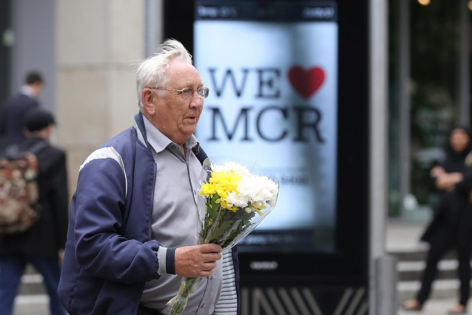  A man carrying a floral tribute walks past a 'We Love MCR' sign which have been put up all around the city after last night's terrorist attack