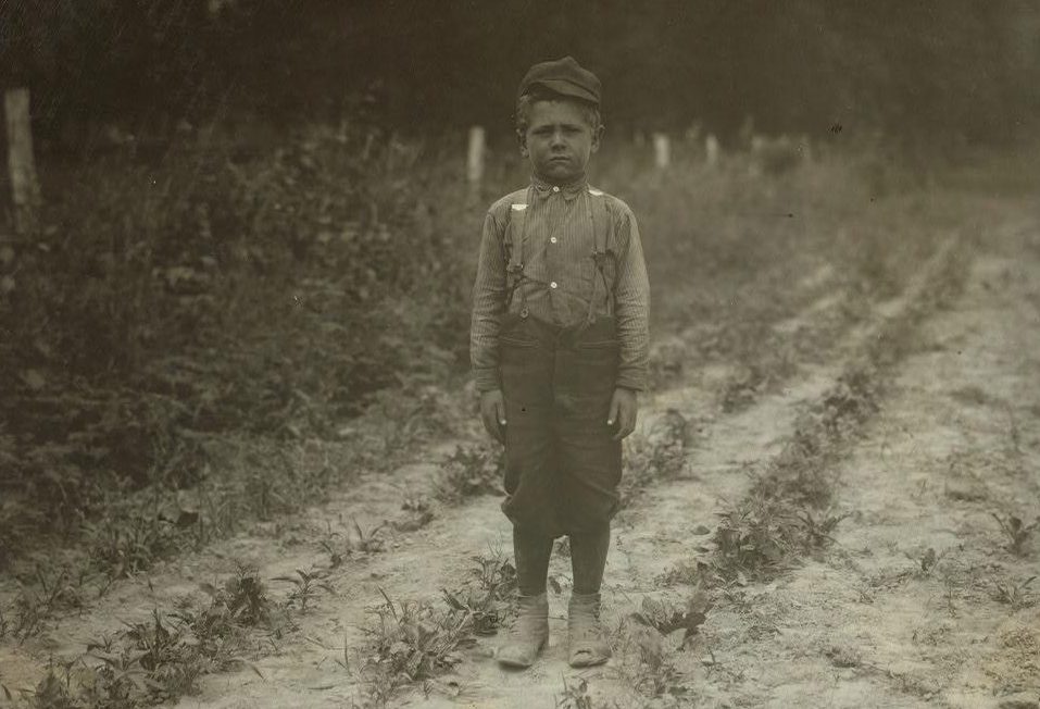  A six-year-old beet worker wearing a cap and dungarees poses between his shifts in Wisconsin, 1915