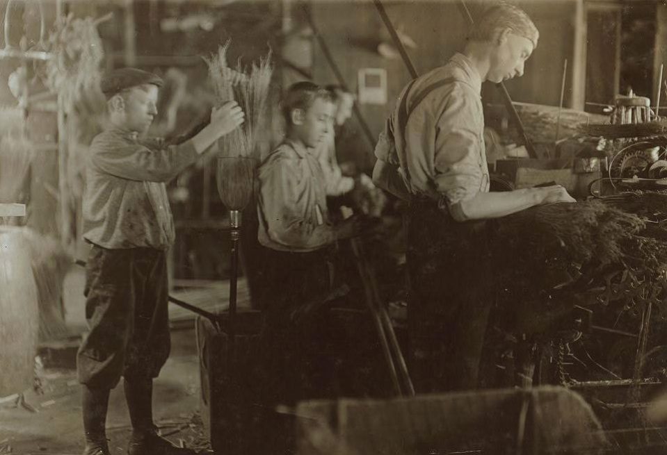  This black and white image shows two youngsters assisting an adult worker at the Broom Machines, Indiana in 1908