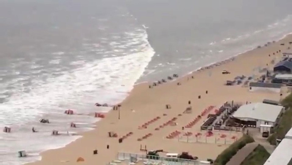 footage shot from the balcony of a flat in Zandvoort, a coastal resort in the Dutch province of North Holland, the wave can be seen sweeping away beach chairs, boats and parasols