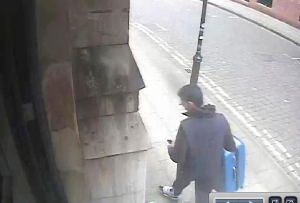  Abedi checks his phone while carrying blue suitcase