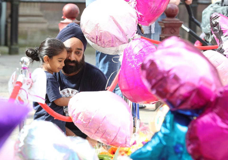 A man and a little girl look on at the flowers and tributes left in St Ann's Square in Manchester ahead of a benefit concert