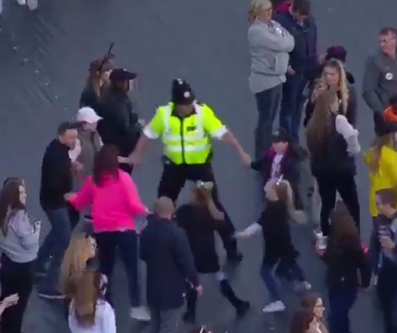 A cop can be seen dancing and holding hands with young concert-goers