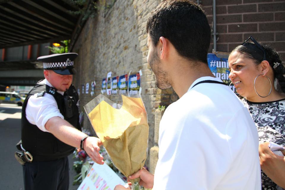  A man hands a bunch of flowers to a police officer across the cordon to lay in tribute at the scene