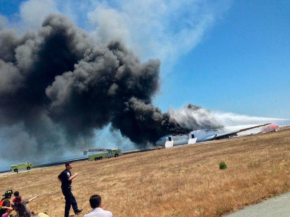 The Asiana Airlines Boeing 777 is engulfed in smoke on the tarmac after crash