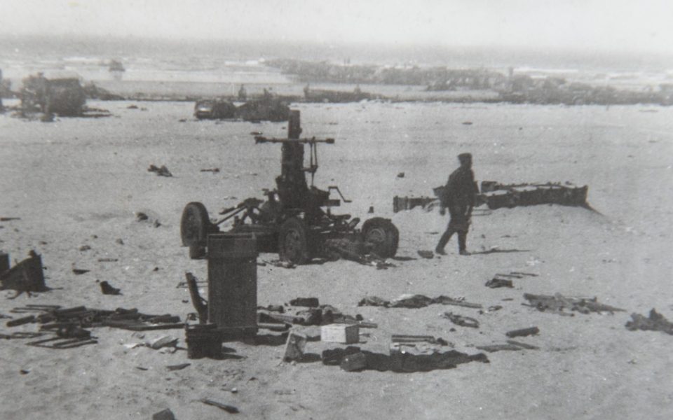  A soldier walking past the axle and wheels of a large military vehicle destroyed by the German guns