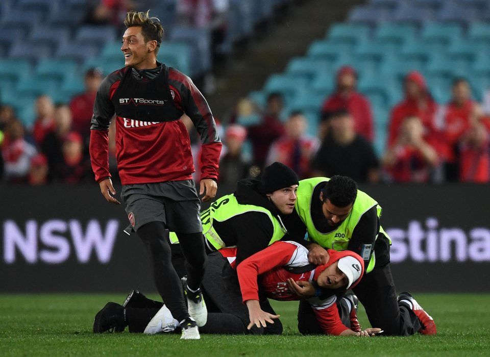  Mesut Ozil grins after a fan was hauled down making a dash for him