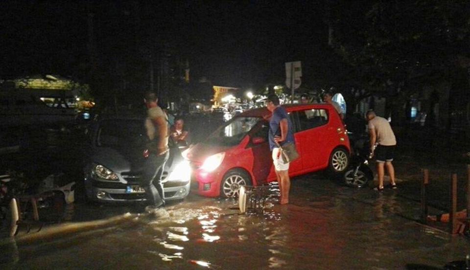  People try to move the cars from a flooded coastal road on the Greek island of Kos