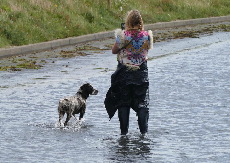  A woman takes a photograph of her dog as they wade through flood waters at high tide at Keyhaven Marshes