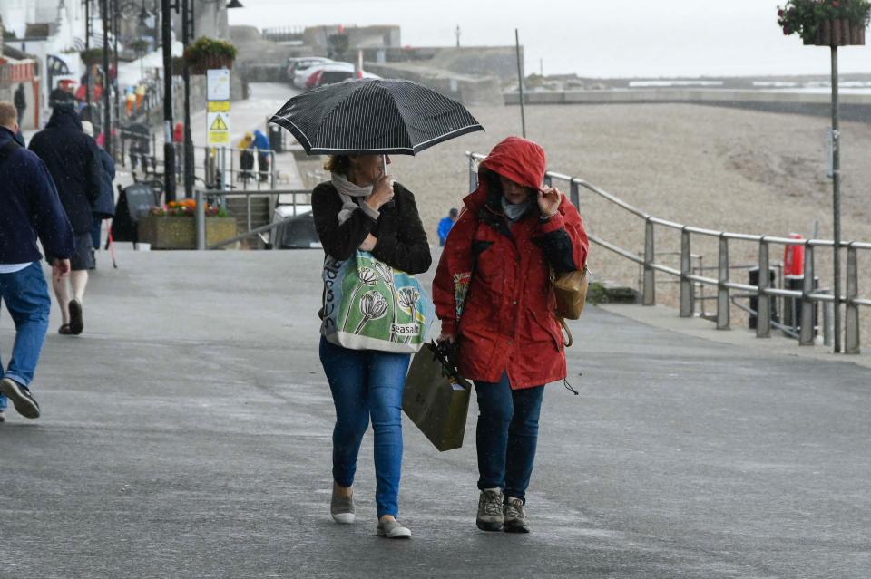  Visitors walking along the seafront with umbrellas up as a shower passes over at the seaside resort of Lyme Regis in Dorset