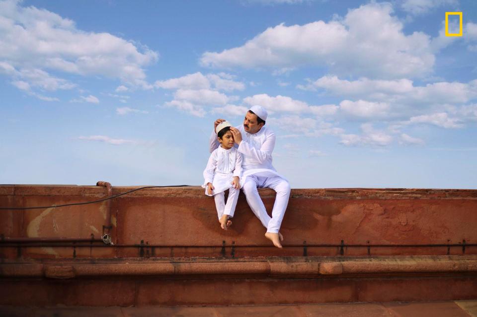  A father and son dressed in traditional white clothing sit at a mosque in New Delhi, India, under a blue sky on Eid al-Fitr, the conclusion of the Islamic holy month of Ramadan