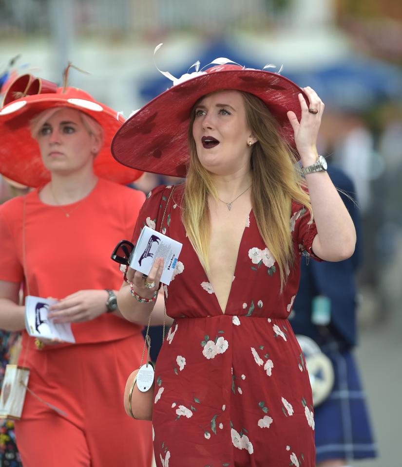  A woman in a low-cut red floral dress held onto her coordinating hat as the breeze picked up