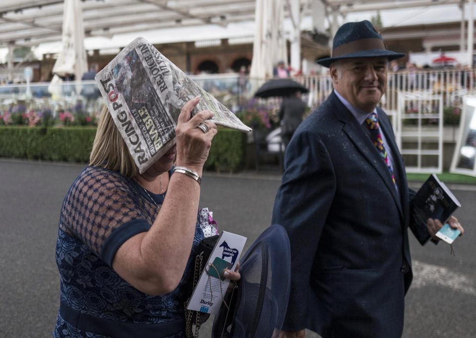  A racegoers uses a soggy edition of The Racing Post to shield herself from the downpour, as her pal in a smart hat looks on