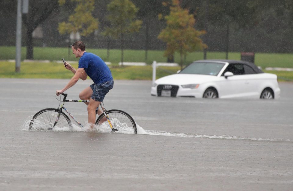 A man checks his phone as he cycles through knee-deep water