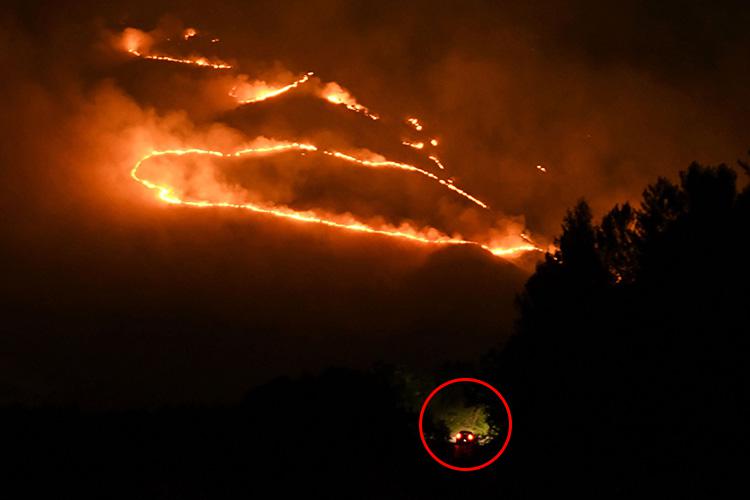 The car, circled, was seen driving on a road as flames and smoke rise from the forest fire near Sarande in the Muzina mountain region, southern Albania