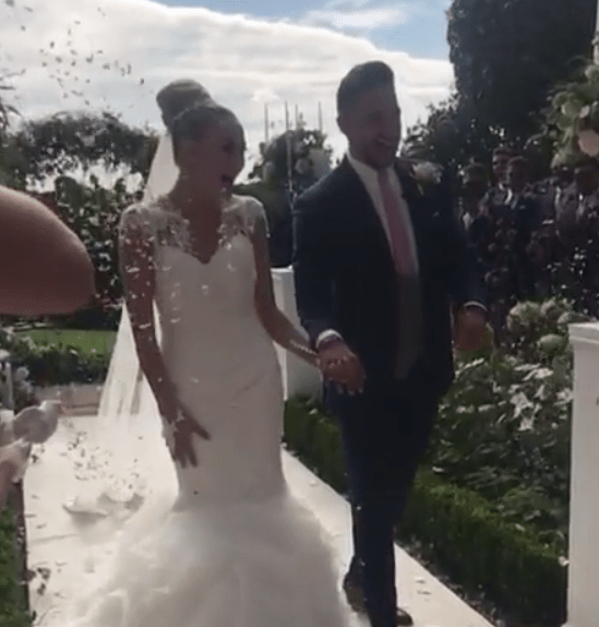 The couple are covered in confetti as they walk down the aisle