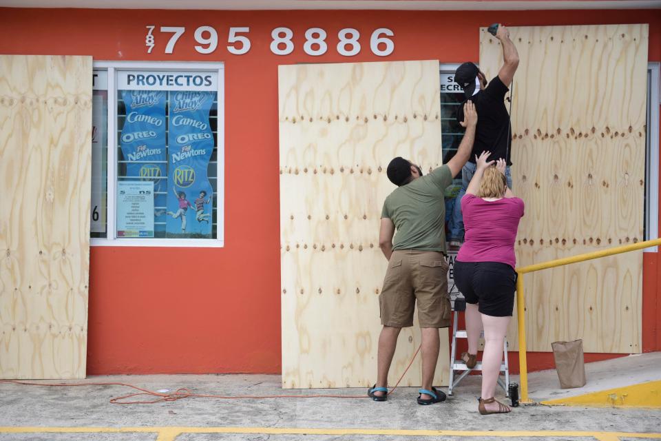  Christopher Rodriguez is supported as he installs wood panels over a storefront window in preparation for Hurricane Irma