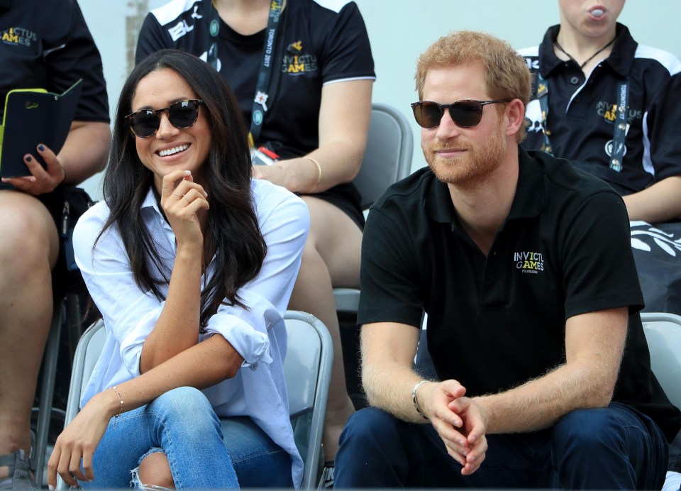 Meghan smiles as she sits next to the prince - who she wasn't able to sit next to yesterday