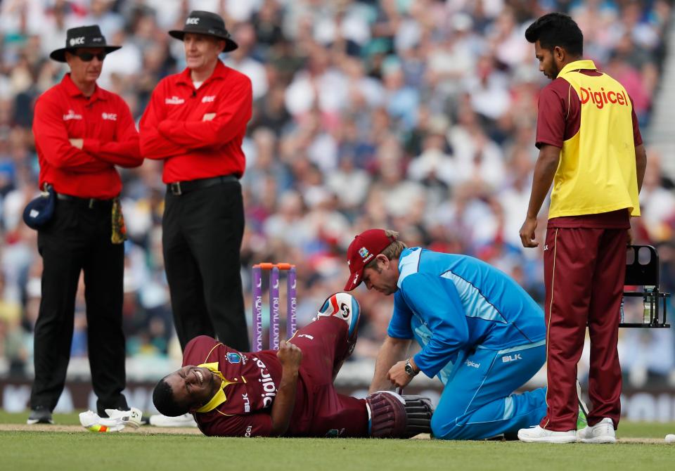 The umpires at the Windies' 12th man look on as Lewis gets treatment 