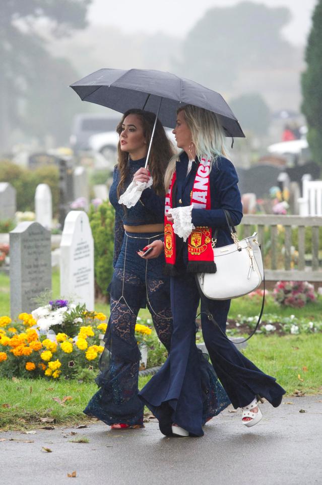  Two mourners walking underneath an umbrella wearing flared trousers at the emotional ceremony