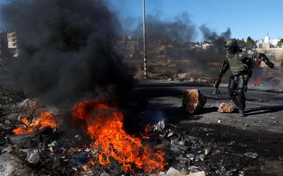  An Israeli border policeman stands next to burning tires as protests over Trump's decision to recognise Jerusalem as Israel's capital continue